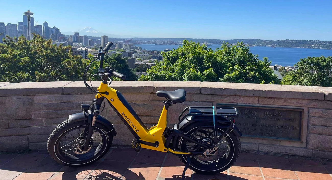 An electric bicycle parked on an observation deck with a view of a city skyline, water, and mountains in the background