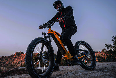 Rider on yellow fat tire electric bike with reflective spokes navigating rocky terrain.