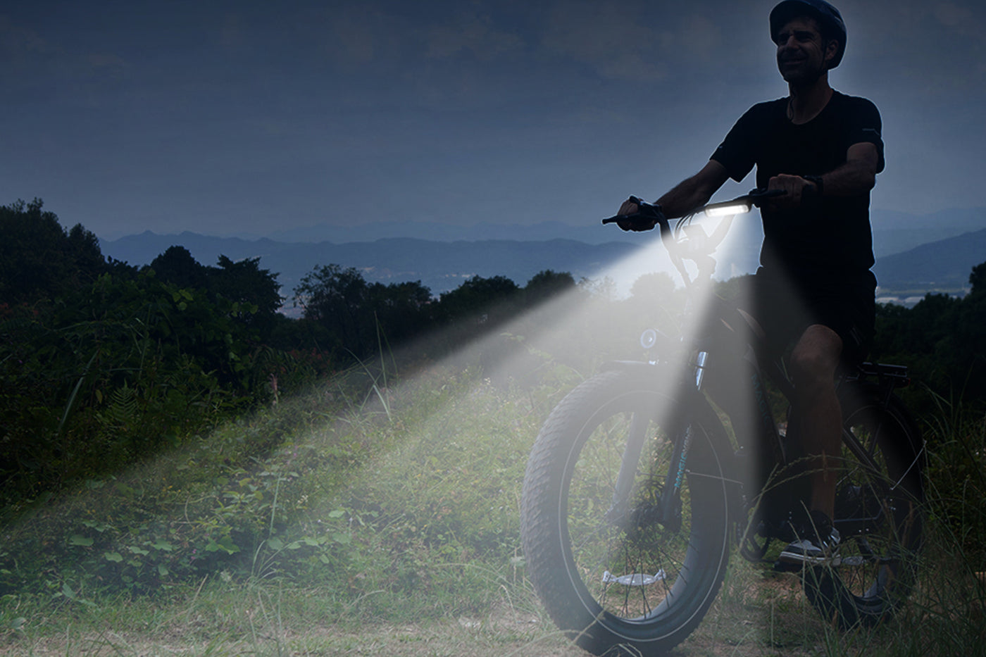 Cyclist riding a fat tire ebike with bright LED headlights illuminating the path.