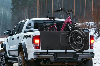 Pink electric bike secured on WestBiking tailgate pad in snowy pickup truck